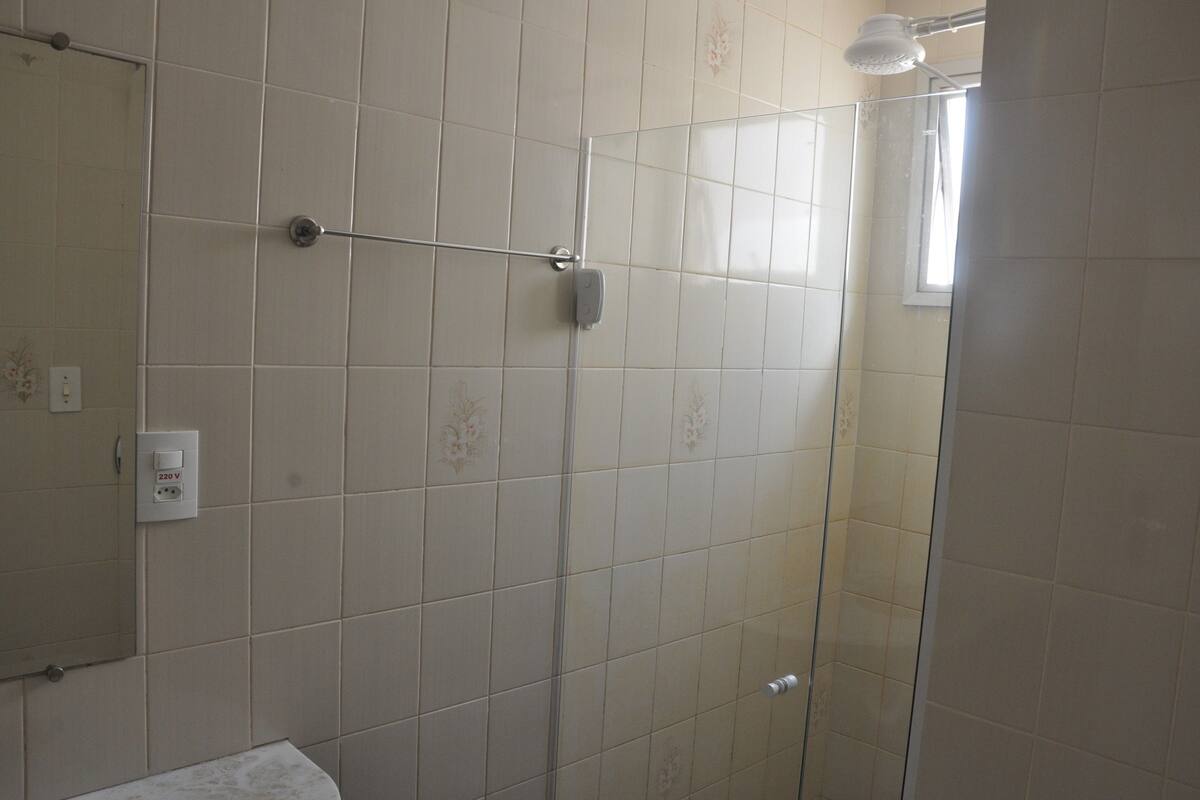 Un baño con cabina de ducha de vidrio, un perchero y un enchufe en la pared.