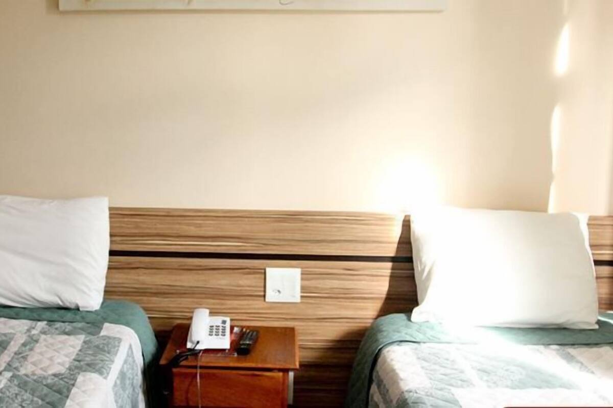 Dos camas individuales con cabeceras de madera, una mesita de noche con teléfono, y un interruptor de luz en la pared.