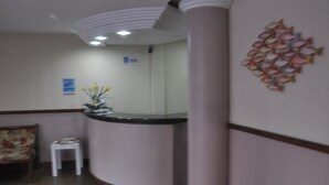A reception area with a curved counter, a small white table, and a wall-mounted fish decoration. - Pousada Raio de Sol (Guarapari)