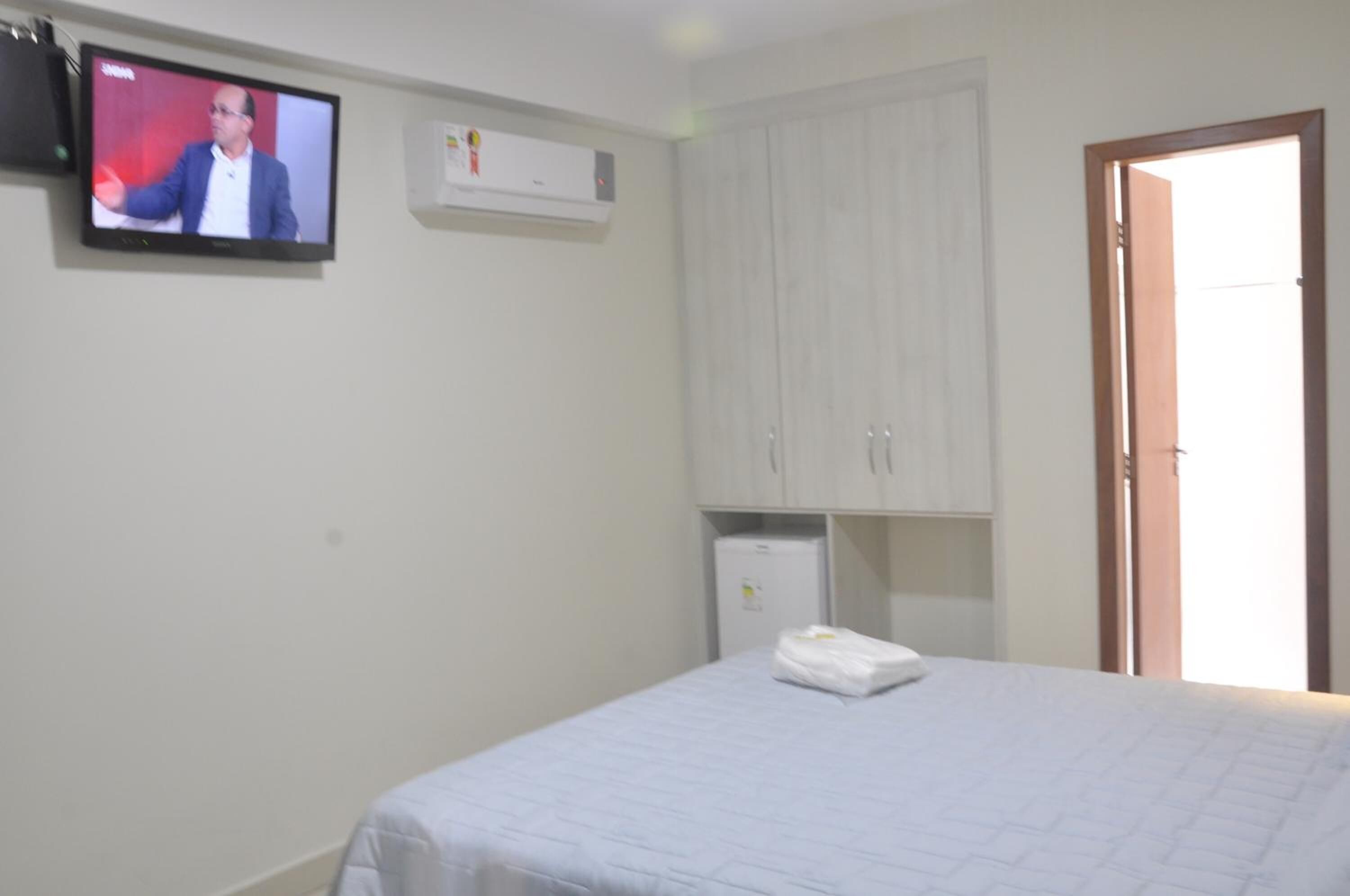 A hotel room with a bed, a television, a wardrobe, and a small refrigerator.