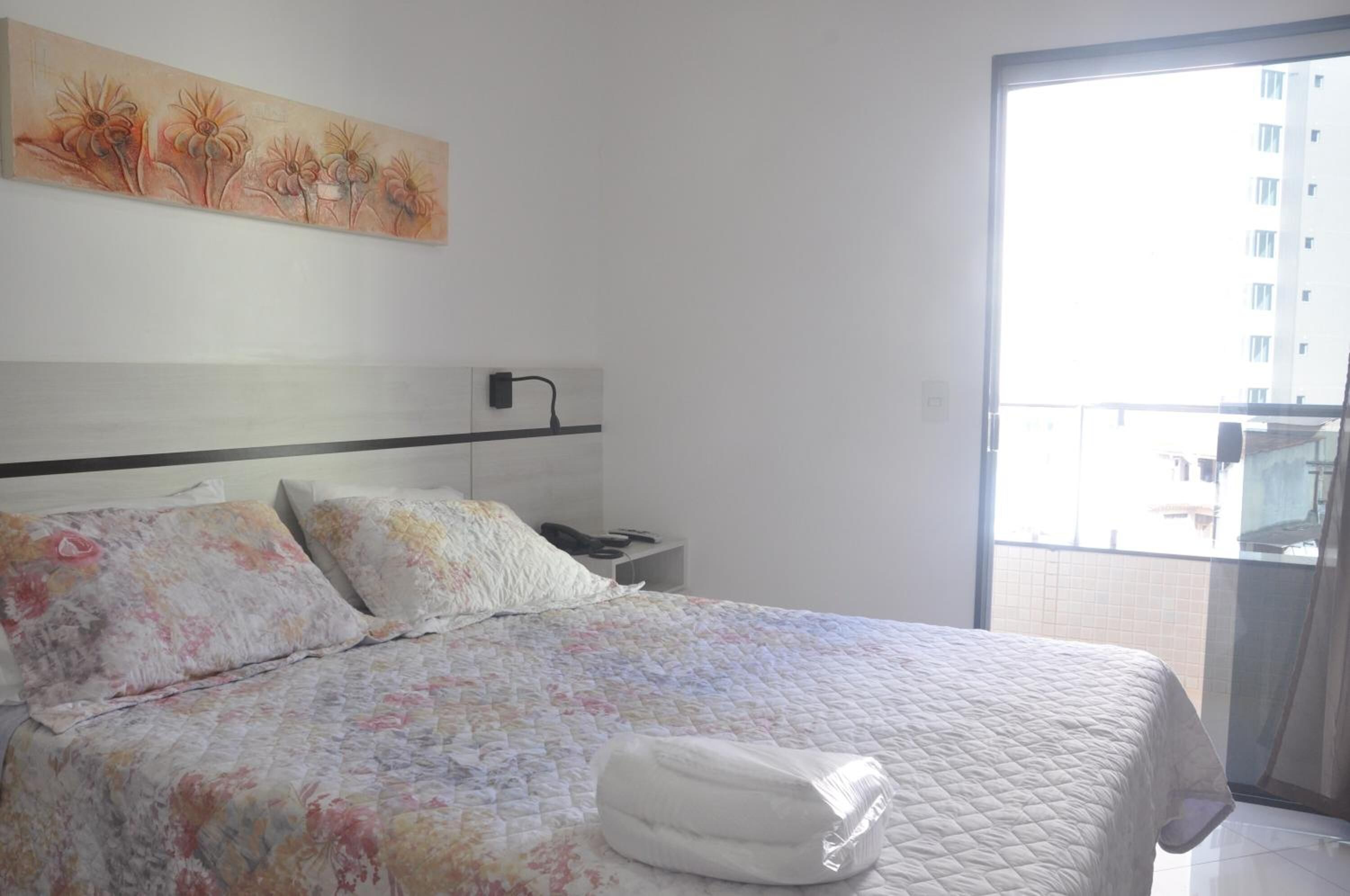 Habitación de hotel con cama, mesita de noche, un cuadro y un balcón con vistas a edificios.