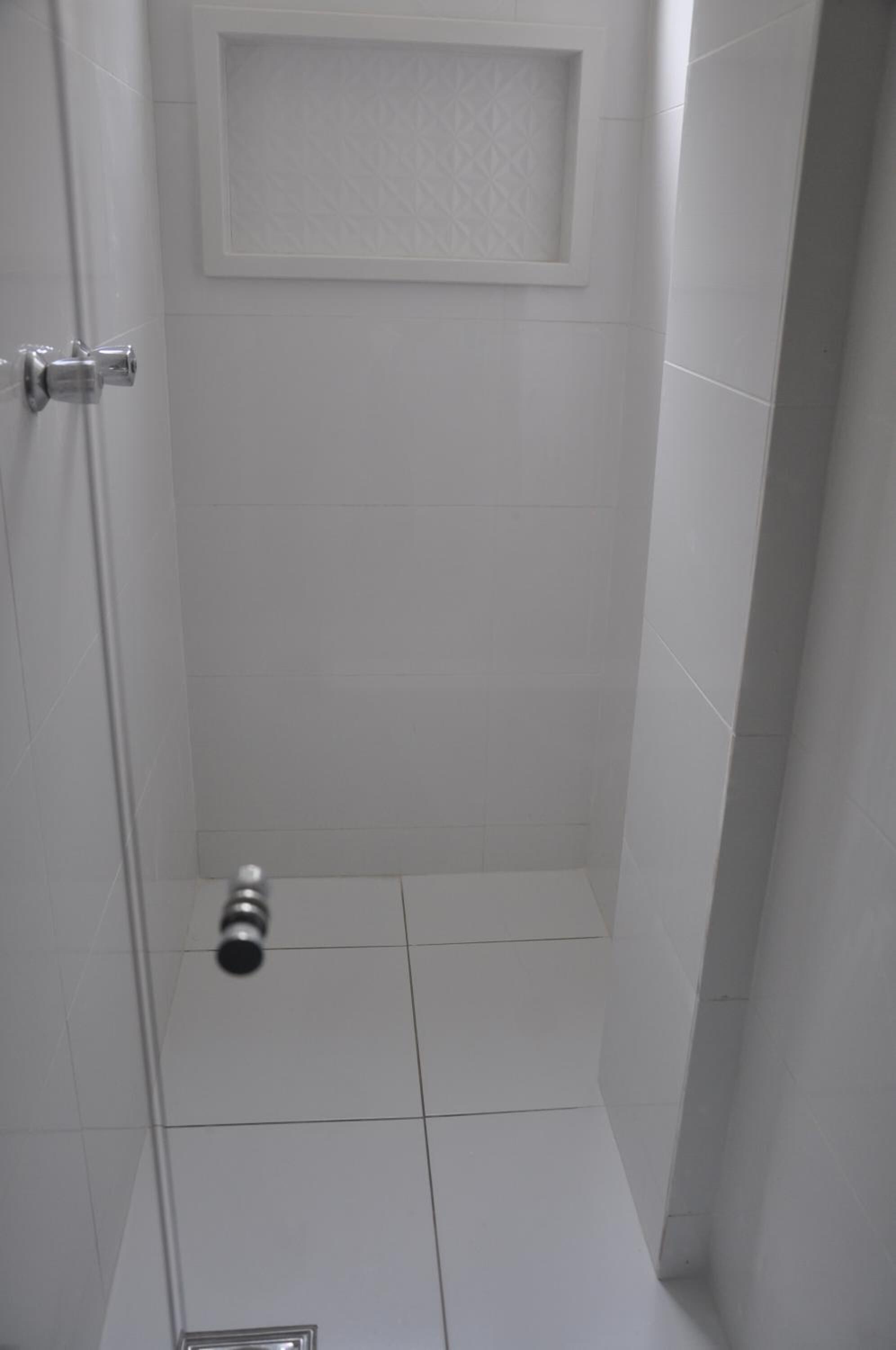 Ein Badezimmer mit weißen Fliesen, einer Duschkabine und einer Tür mit Griff.