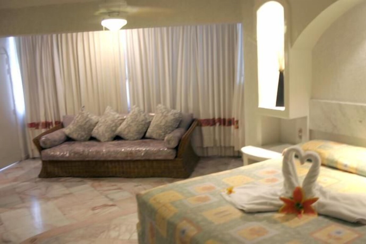 A room with a sofa, a bed with a heart-shaped pillow, and a window with curtains.
