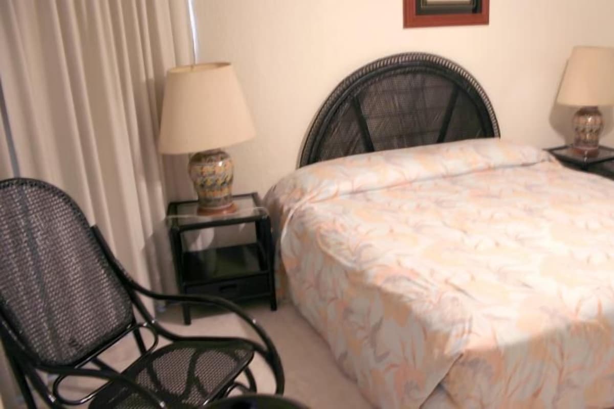 A hotel room with a bed, two chairs, a nightstand with a lamp, and a wall-mounted picture frame.