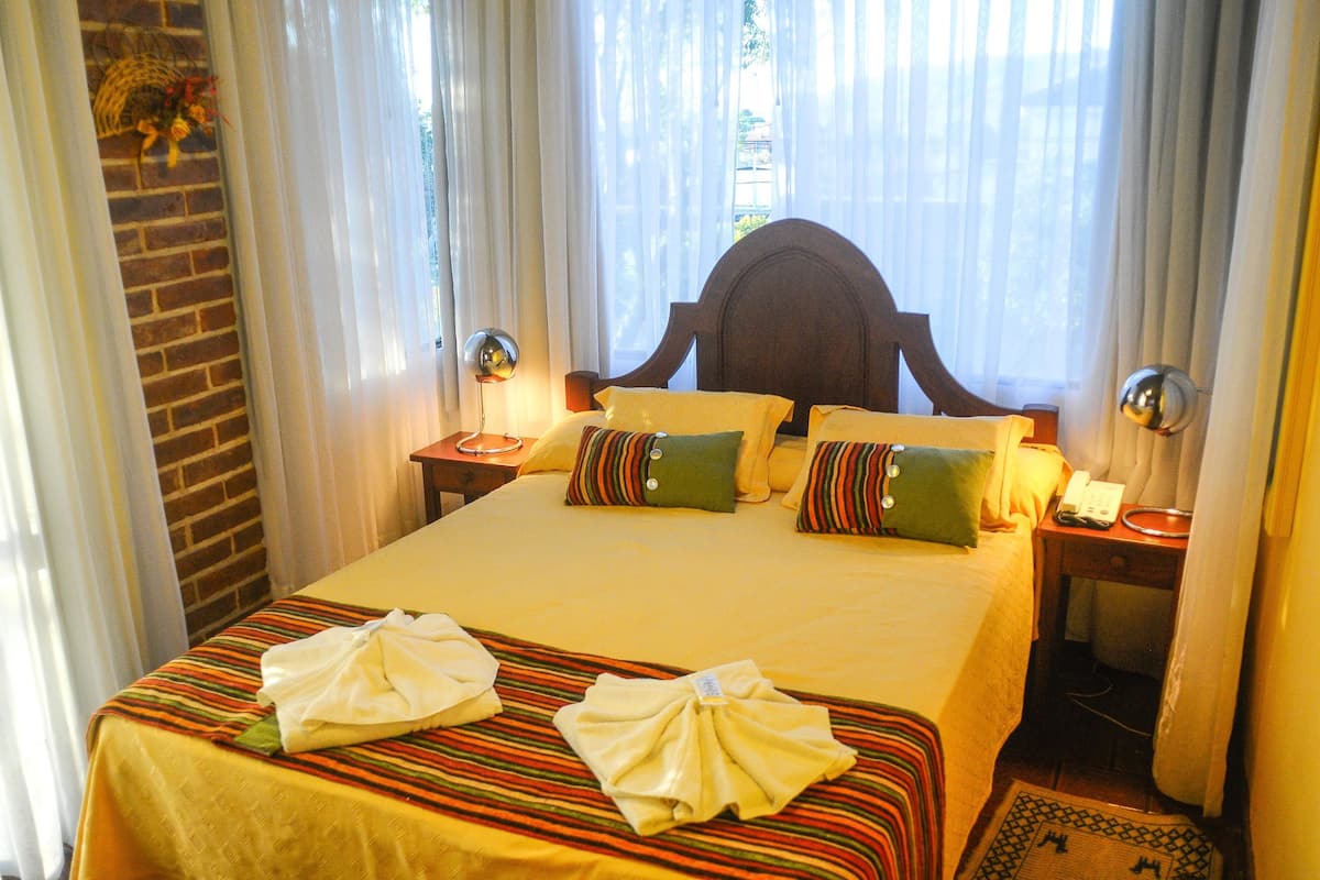 A hotel room with a large bed, striped bedspread, two pillows, a nightstand with a lamp, and a telephone.