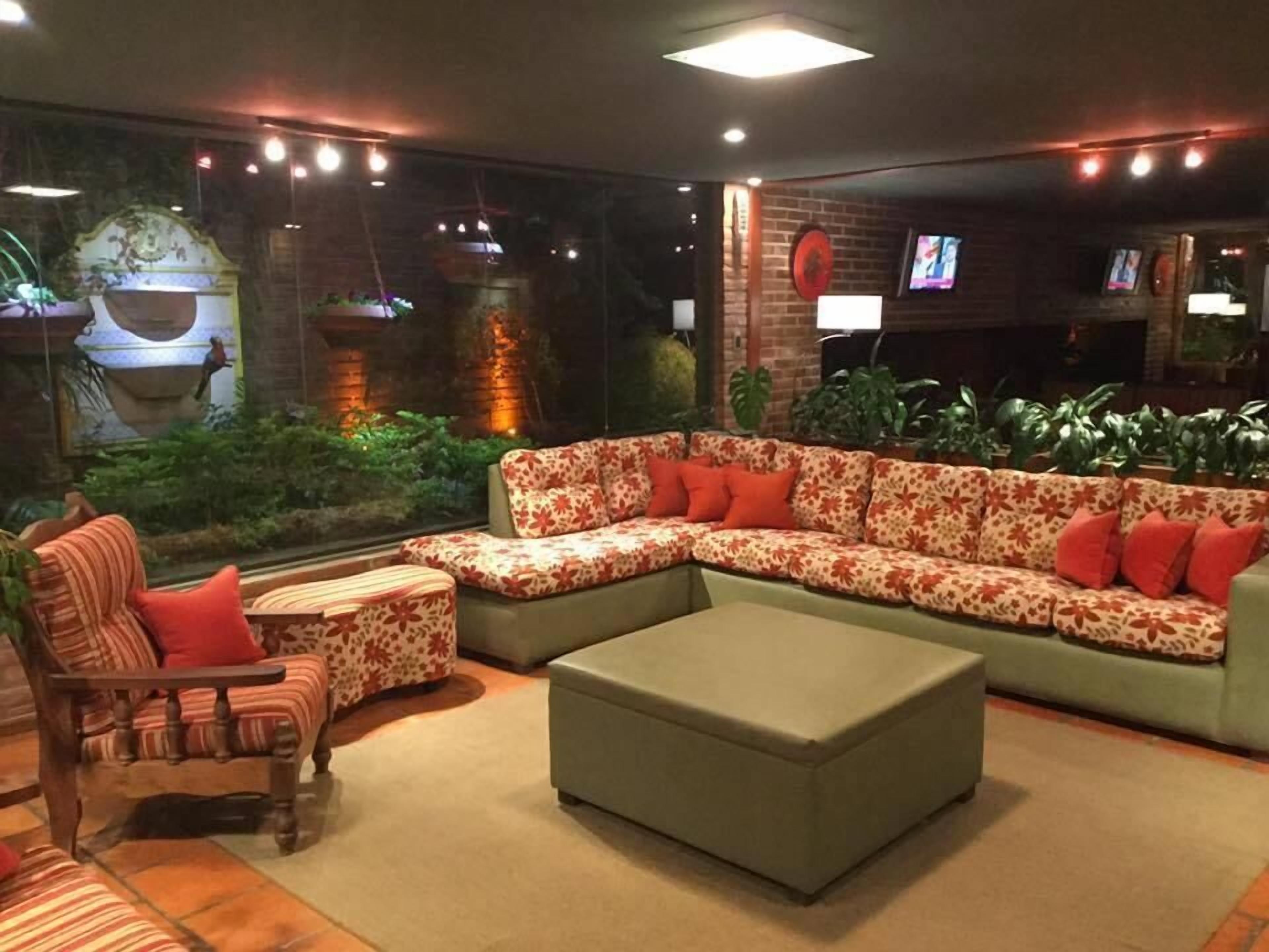 Un rincón de sala acogedor con un sofá modular, un reposapiés pequeño y un sillón. Hay un televisor montado en la pared y una ventana con vistas a zonas verdes.