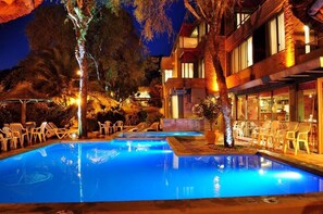 A nighttime pool area with lounge chairs and a building with multiple windows. - Hotel Costa Azul (Villa Carlos Paz)