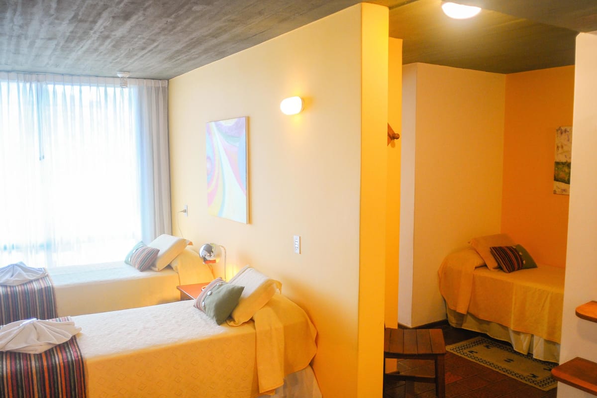 A hotel room with two beds, a window with curtains, a painting on the wall, and a small rug.