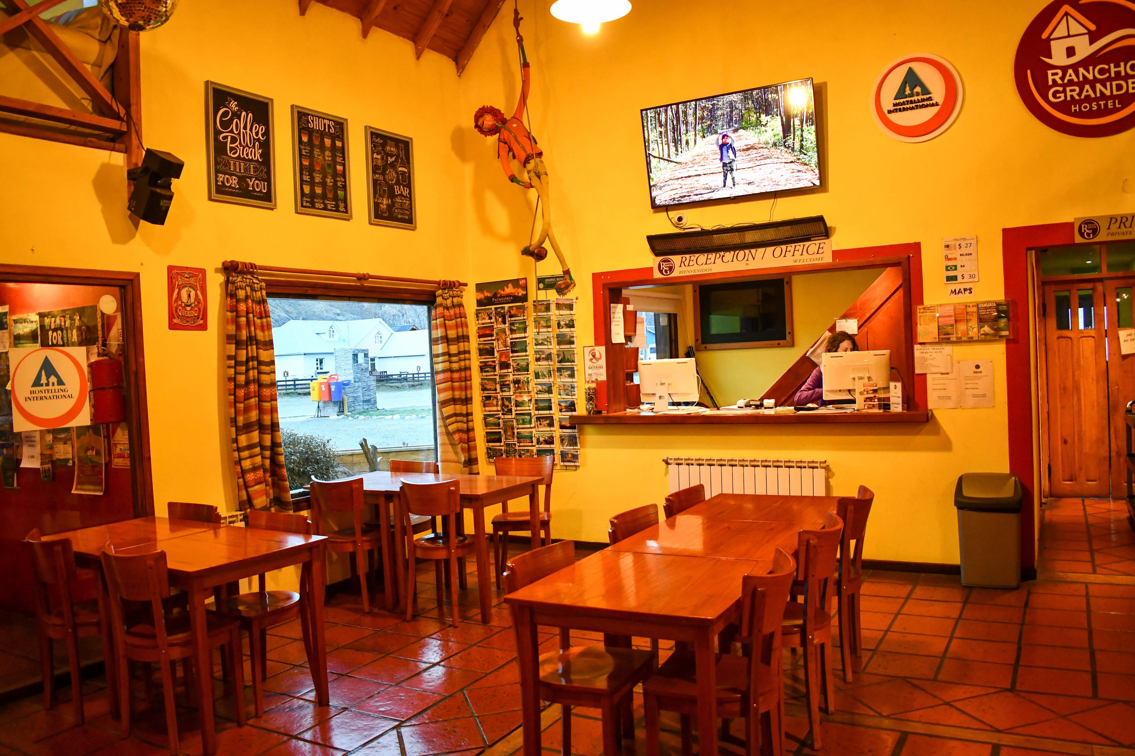 A restaurant with wooden tables and chairs, a reception desk, and a television displaying a forest scene.