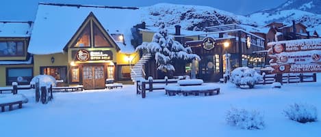 Un espacio al aire libre cubierto de nieve con un edificio que muestra un letrero para restaurante y hostal.