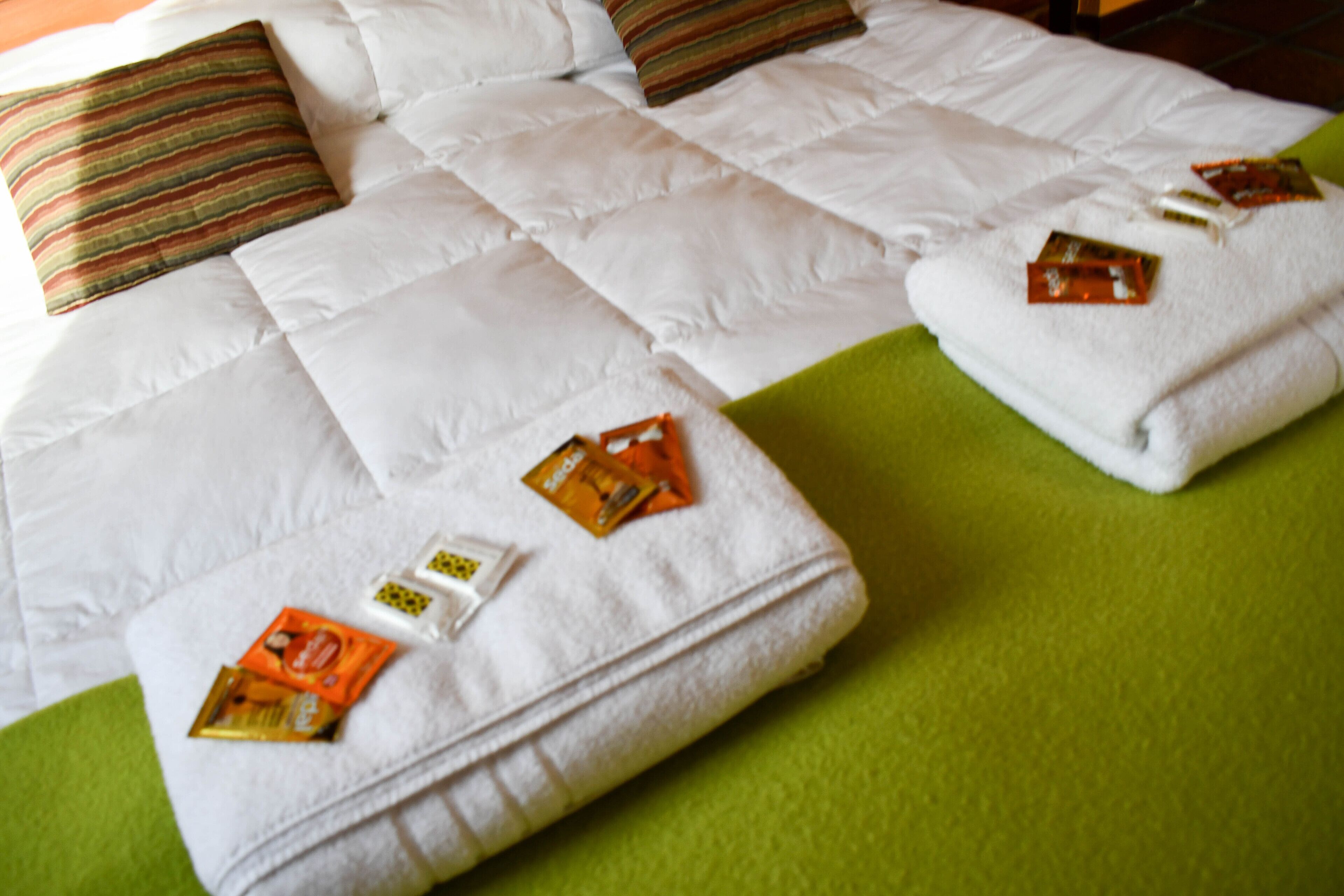 Een netjes opgemaakt bed met kussens, een groene deken en diverse toiletartikelen op de kussens.