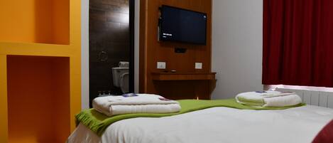 Ein Hotelzimmer mit Bett, einem an der Wand befestigten Fernseher und einem durch eine offene Tür einsehbaren Badezimmer.