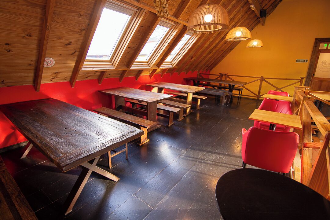 Un'accogliente sala da pranzo in stile rustico, con tavoli e panche in legno, soffitti alti con finestre a lucernario e un'atmosfera calda e invitante.