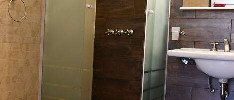 A modern bathroom with a glass-enclosed shower, a white pedestal sink, and a bidet.