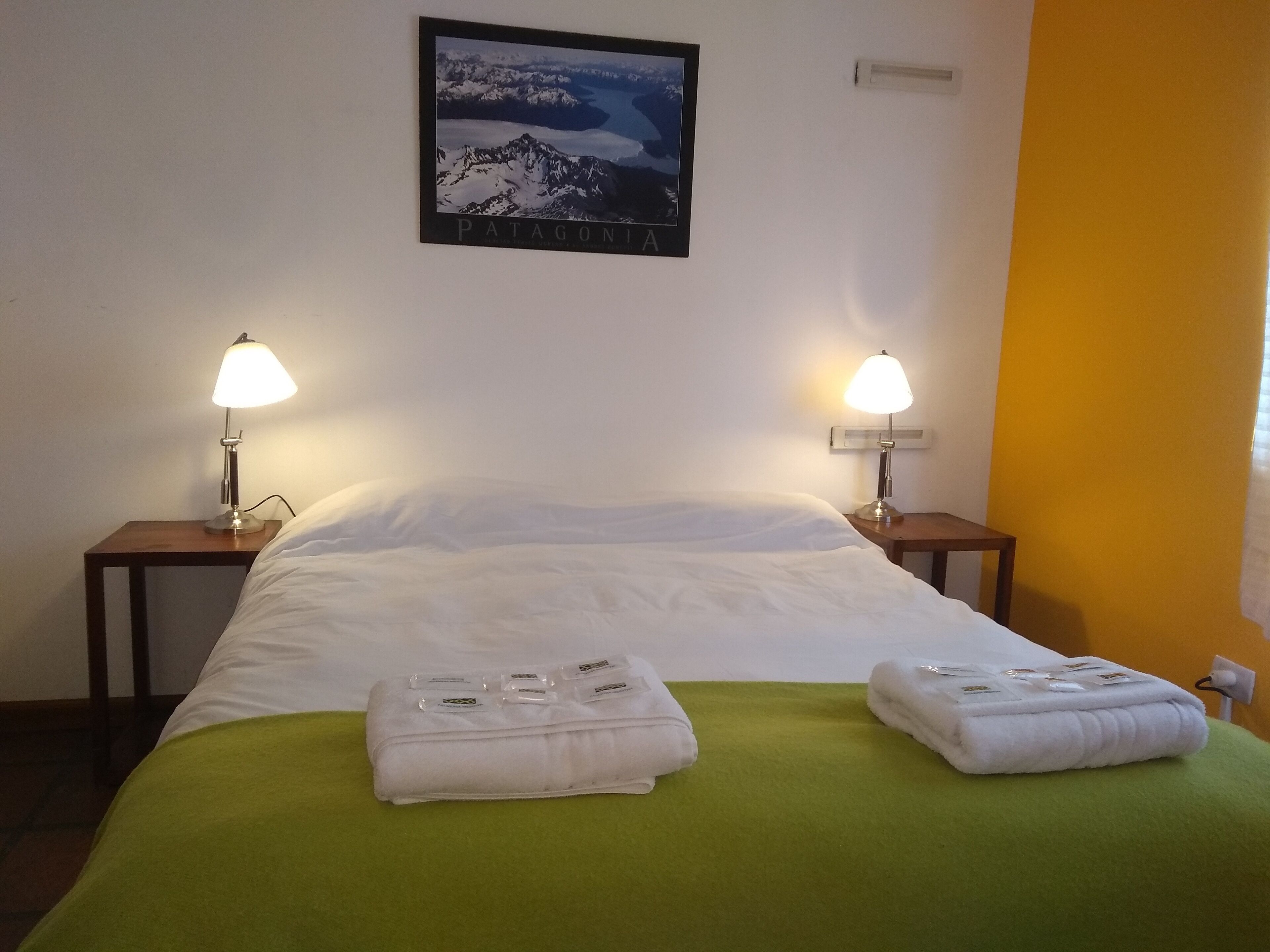 Ein Hotelzimmer mit einem Bett, zwei Nachttischlampen, einem gerahmten Bild an der Wand und zwei gefalteten Handtüchern auf dem Bett.