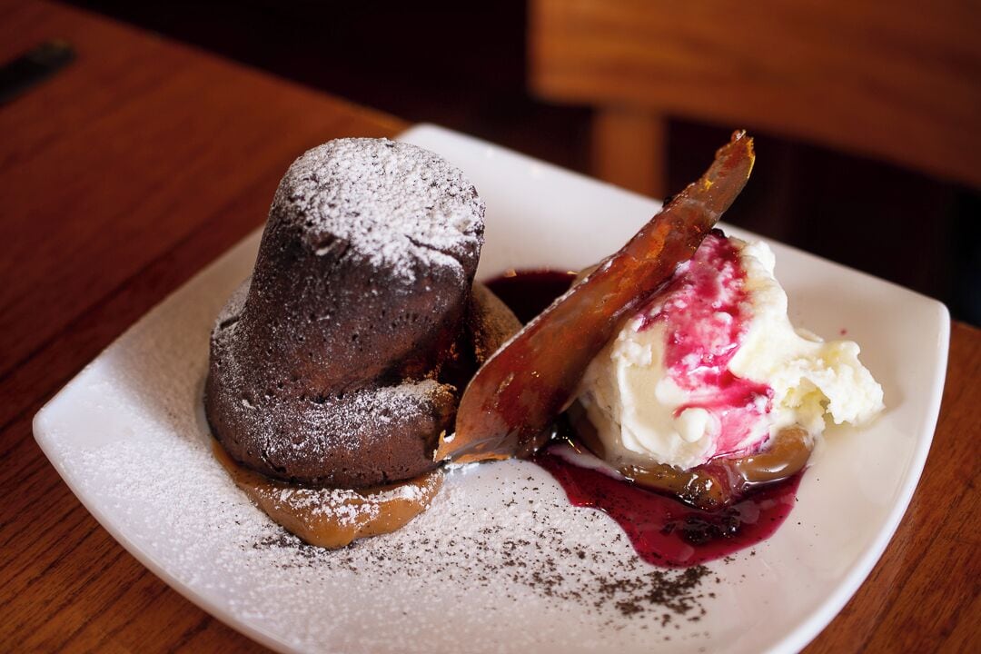 Une assiette de dessert avec un fondant au chocolat et une boule de glace à la vanille, le tout accompagné d’une compote de fruits rouges.