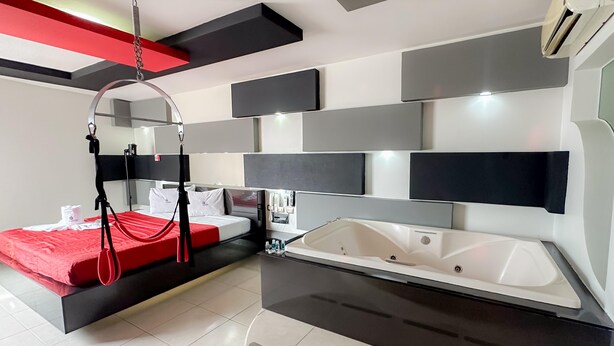 A modern hotel room with a bed, a large mirror, a built-in bathtub, and a red hanging chair. - Auto-hotel Mediterraneo (Banderilla)