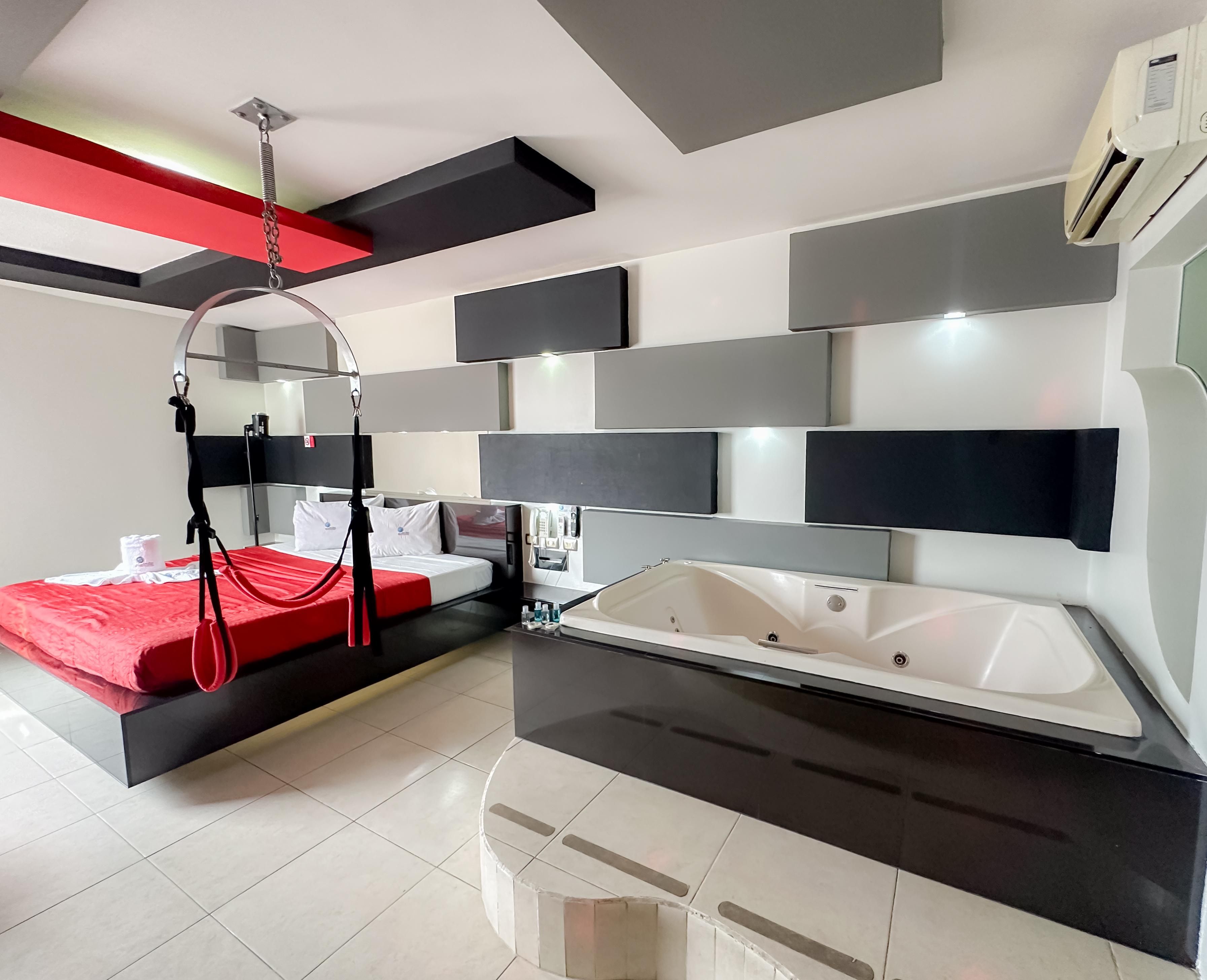 Una habitación de hotel moderna con una cama, un espejo grande, una bañera integrada y una silla colgante roja.