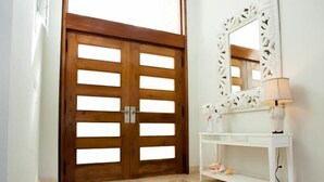 A hallway with a wooden door, a white console table with a lamp, and a decorative mirror. - Villa Ibiza - Cocotal 3.5 Hab (Punta Cana)