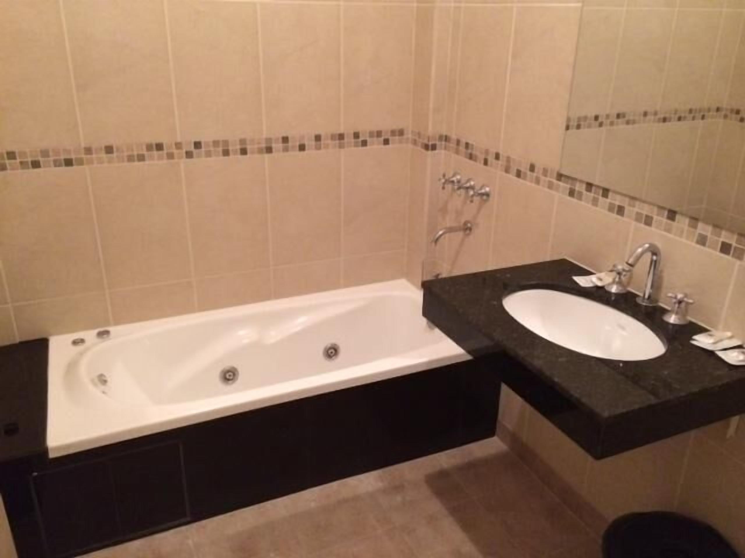 Un baño con una bañera blanca, un lavabo negro y un espejo sobre el lavabo.