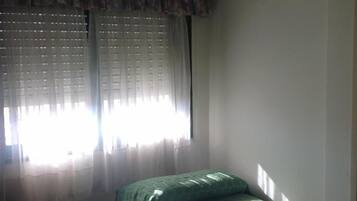 A room with a bed, a window with sheer curtains, and a wall.