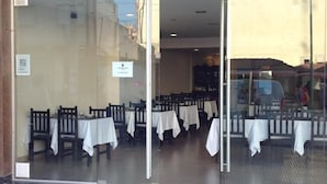 A restaurant with tables set for dining, a sign indicating a restaurant name, and a view of the street outside. - Hotel San Carlos (Termas de Rio Hondo)