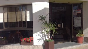 A building with large windows, a door with a sign, and potted plants outside. - Hotel San Carlos (Termas de Rio Hondo)