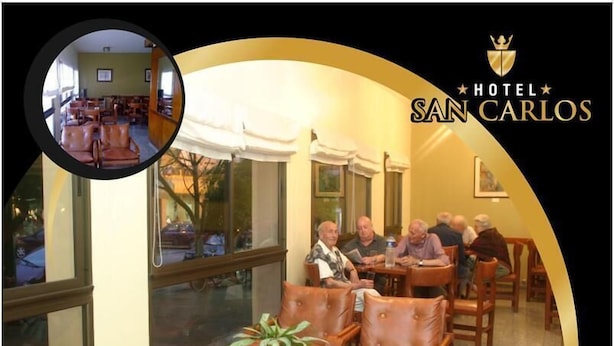 A hotel lobby with leather sofas, a dining area, and a large window. - Hotel San Carlos (Termas de Rio Hondo)