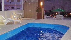 An outdoor swimming pool with lounge chairs and a table, surrounded by a low wall and a potted plant. - Hotel San Carlos (Termas de Rio Hondo)