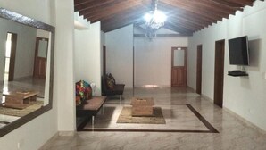 A spacious living area with a high ceiling, a chandelier, a sofa, a coffee table, and a flat-screen TV mounted on the wall. - Hotel Porton Colonial (Medellín)