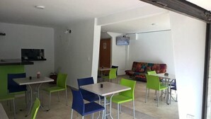 A dining area with tables and chairs, a sofa, and a television. - Hotel Porton Colonial (Medellín)