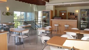 A modern dining area with multiple tables and chairs, a bar area with stools, and a view of the outdoors through large windows.