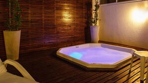 A hot tub with a wooden deck and potted plants, set against a wall with horizontal wooden slats.