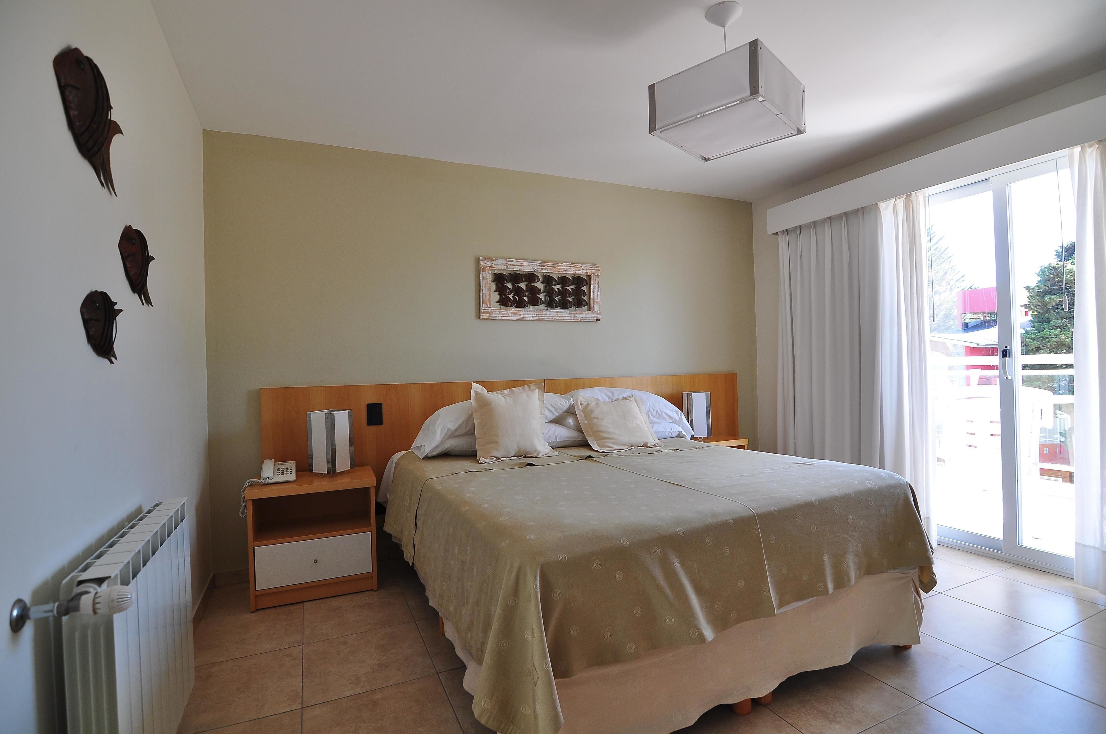 Un dormitorio con cama, mesita de noche, una obra de arte en la pared y vistas a través de una ventana.