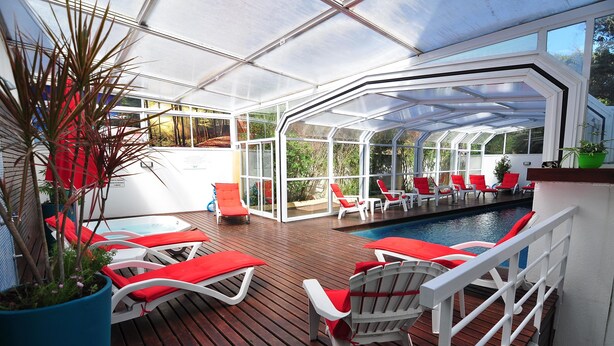 A covered outdoor deck with red lounge chairs and a pool.