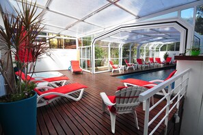 Une terrasse extérieure couverte, dotée de chaises longues rouges et d’une piscine.