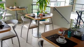 Un café moderno con varias mesas y sillas, un ventanal con vistas a zonas verdes y una escalera con barandilla.