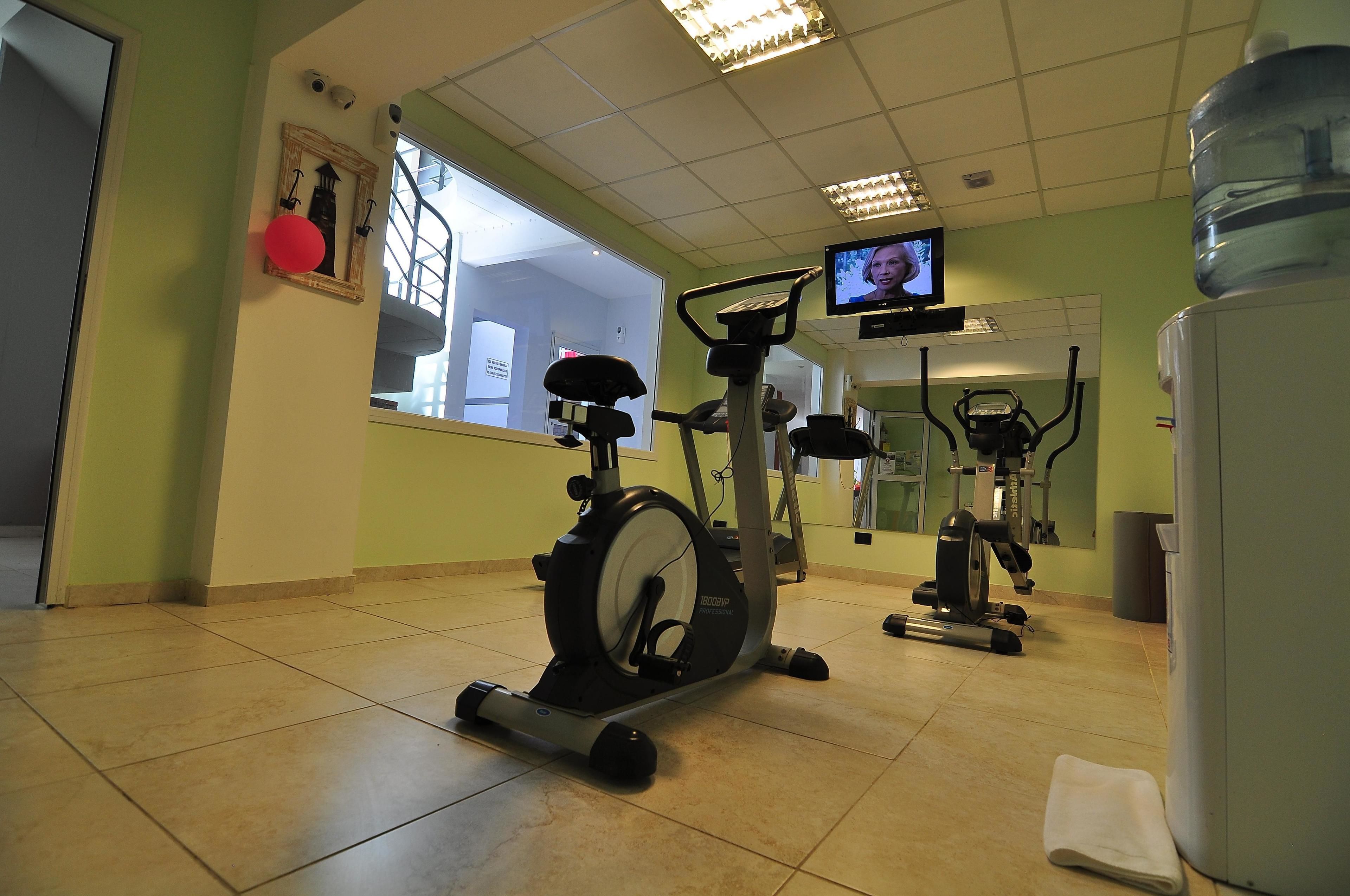A gym with exercise equipment, a water dispenser, and a television on the wall.