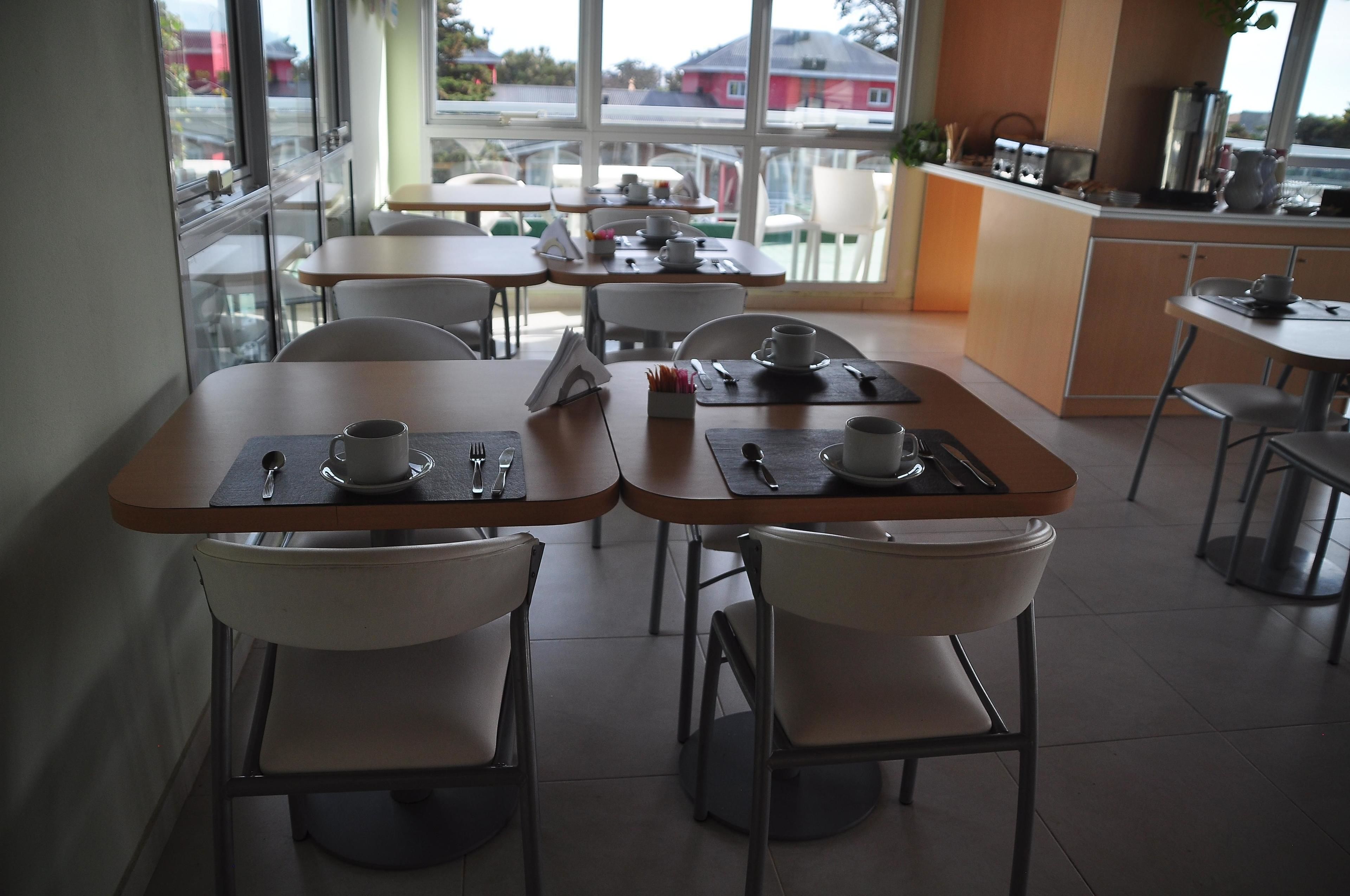 A cafe with tables and chairs, a kitchen area, and large windows.