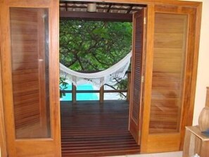 Une porte en bois donne accès à un espace extérieur abrité, où se trouvent un hamac et d’où l’on peut admirer un arbre.