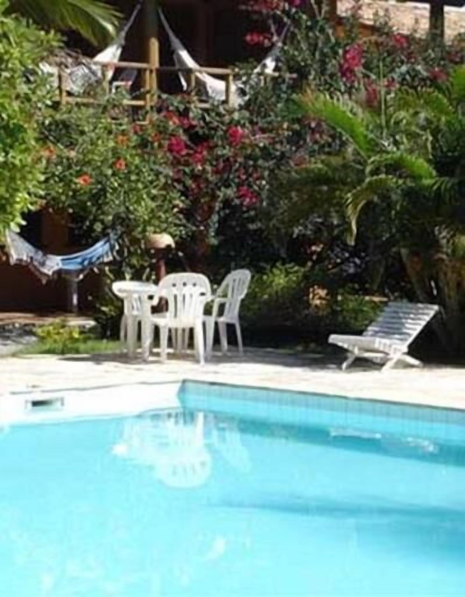 Piscina com espreguiçadeira e mesa com cadeiras.
