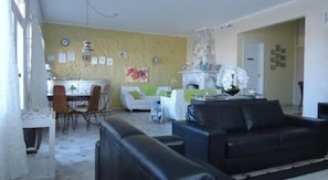 A living room with a black sofa, a white couch, and a dining area with chairs and a table. - Solar Dom Kido Pousada (Torres)