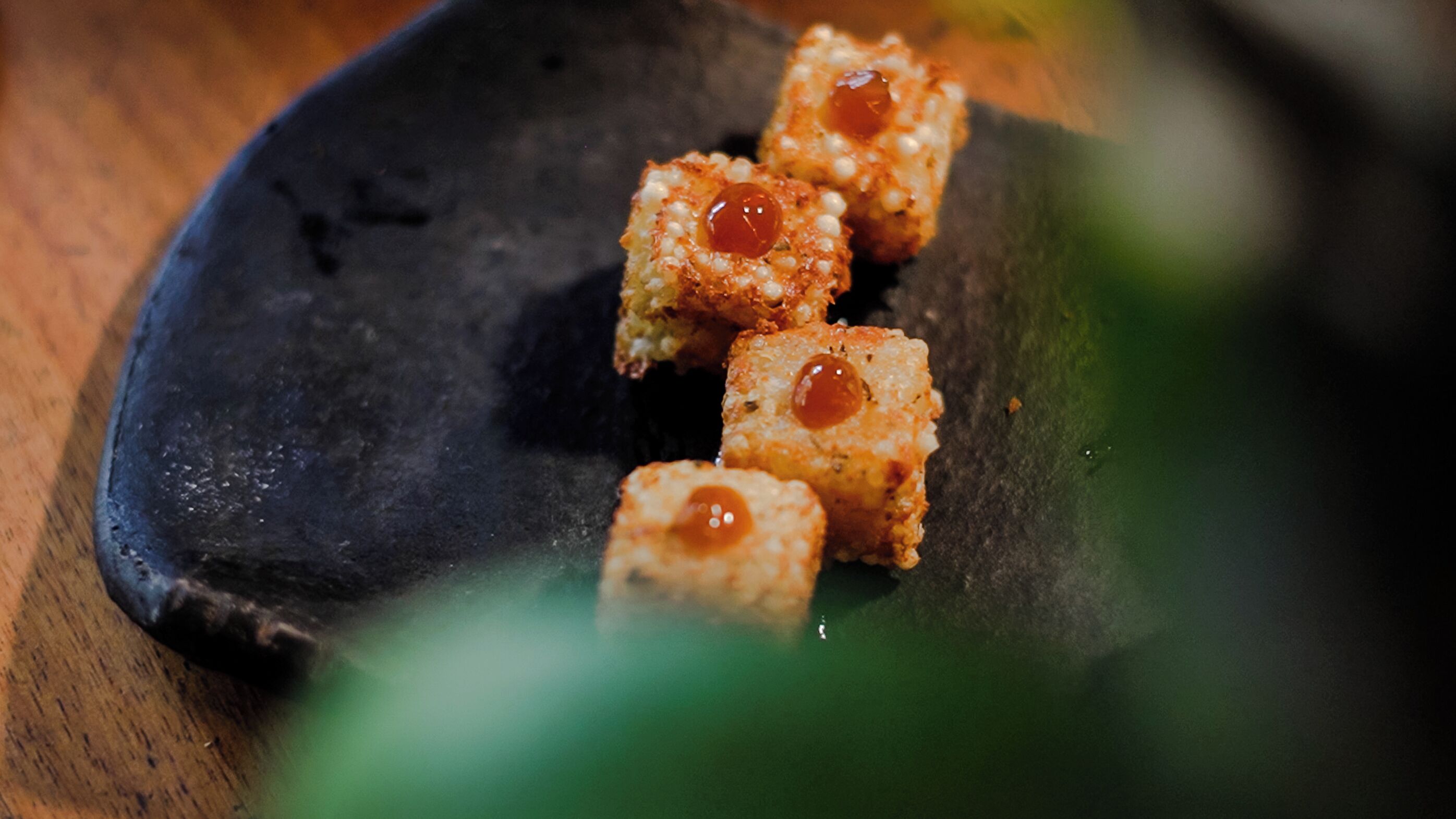 Un plato negro con cuatro porciones cuadradas, cada una cubierta con salsa roja.