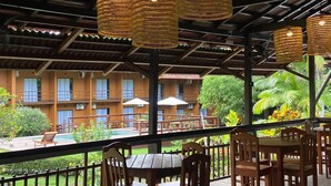 An outdoor dining area with wooden tables and chairs, a wooden deck, and a view of a building with multiple windows and a balcony.