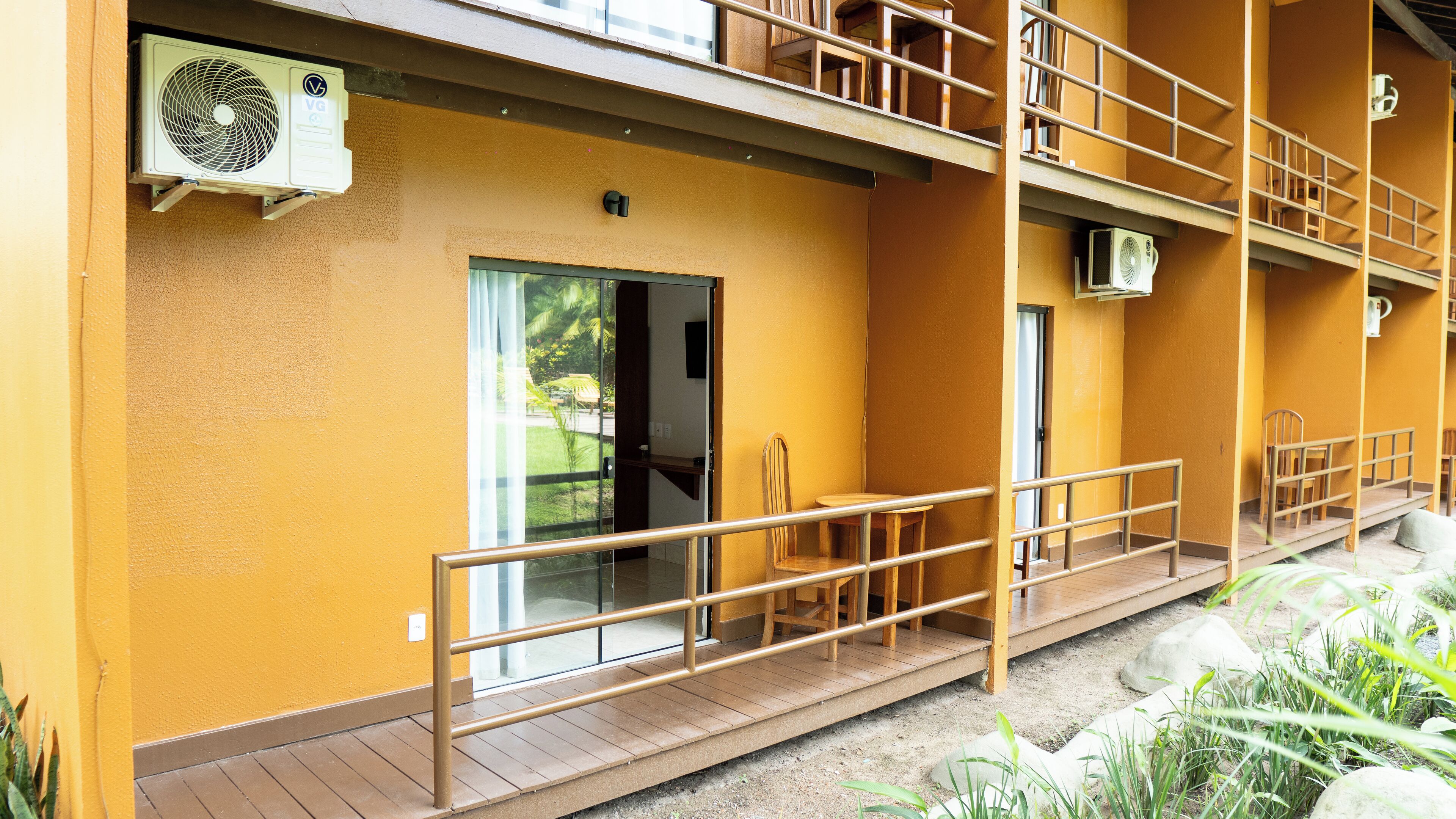 A building with a yellow exterior, a wooden balcony, and a door leading to an interior space.