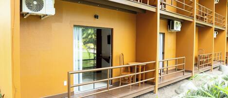 Un edificio con fachada amarilla, un balcón de madera y una puerta que da a un espacio interior.