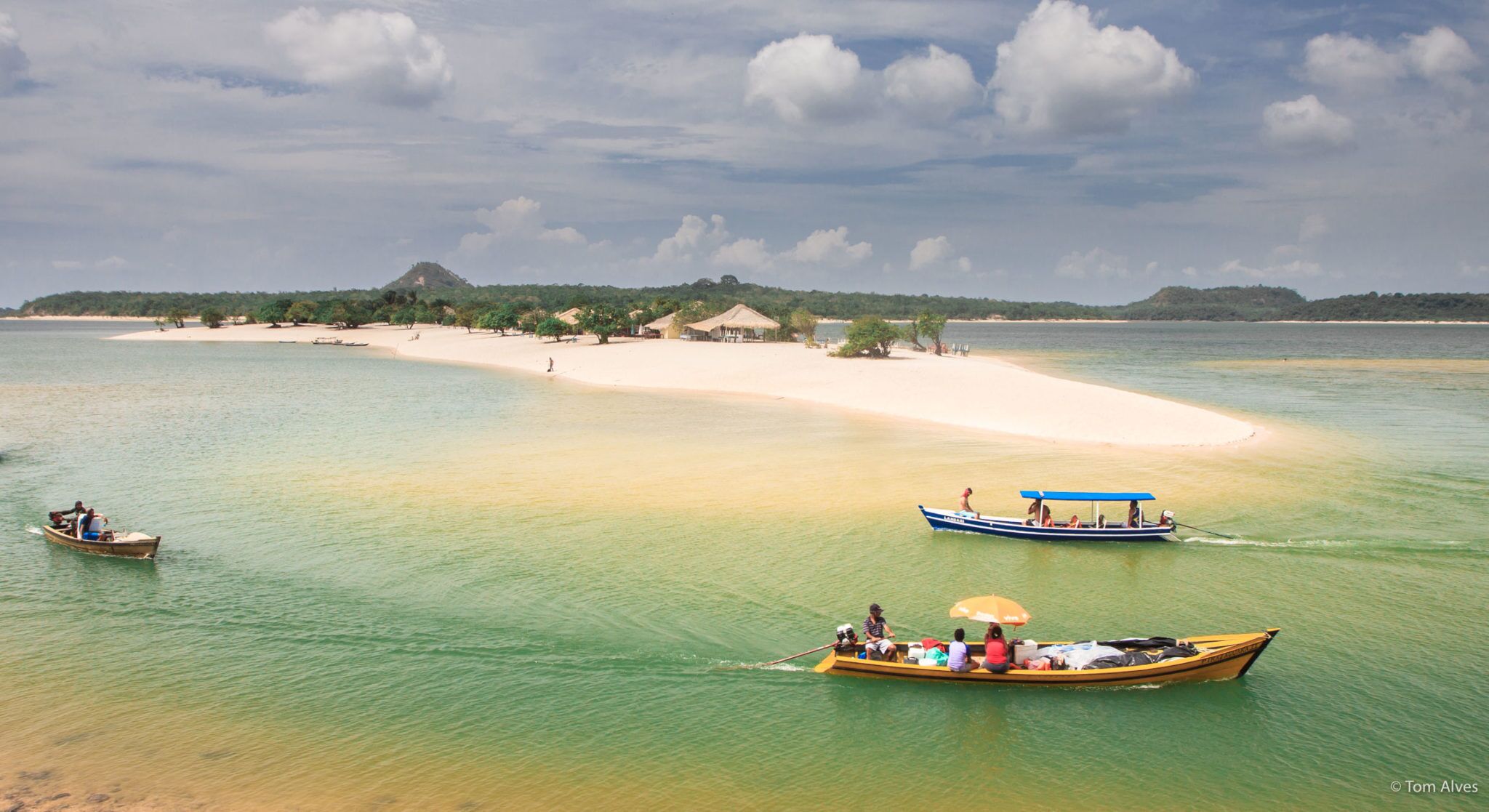Una playa tropical con aguas turquesas cristalinas, una orilla arenosa y algunas embarcaciones.