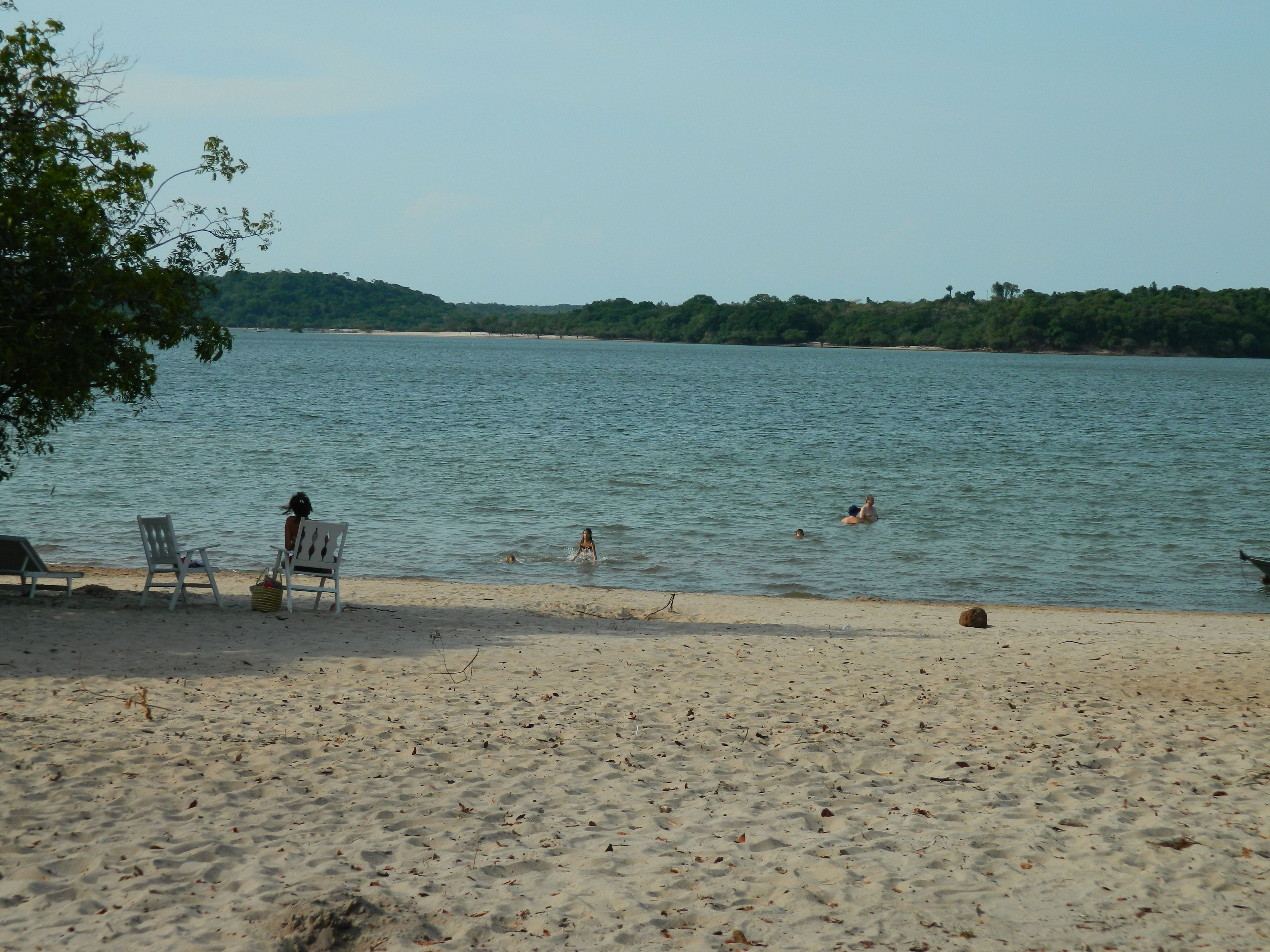A beach with a few people swimming and a few chairs on the sand.