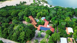 An aerial view of a property with dense greenery, a swimming pool, and a building with solar panels.