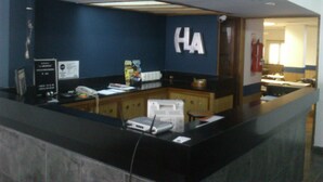A hotel reception desk with a dark blue wall, a sign with 'HA' letters, a fire extinguisher, and a counter with various items. - Hotel La Argentina (San Bernardo del Tuyú)